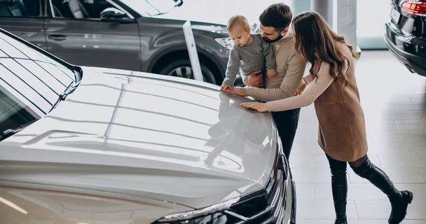 A young couple and their small child, looking at a used car in a dealership.