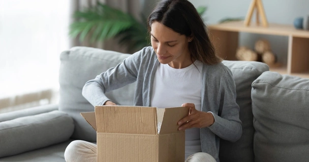 Young woman sitting on couch unpacking cardboard box