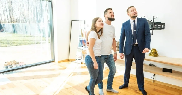 A young couple being shown around a house by a salesman.