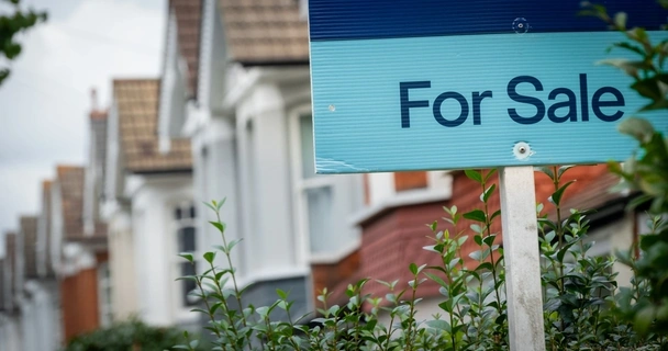For sale sign with a row of houses behind