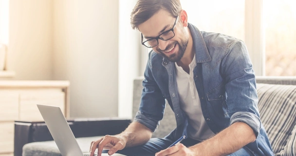 man on laptop smiling and making notes