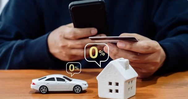Close up of a man with his phone and credit card with a model home and a model car in front of him with 0% bubbles around the models
