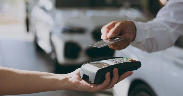 someone paying contactless with their credit card, with a car dealership in the background