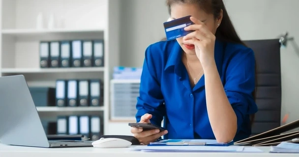 Woman looking at her phone and holding up a credit card
