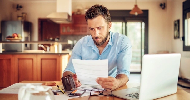 Man sat at the table looking through documents with his wallet and laptop open