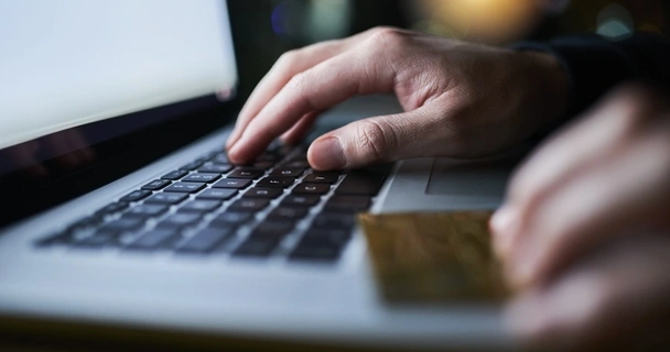 zoomed in on a man using a laptop with a credit card in his hand.