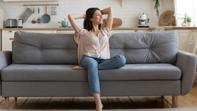 Happy single lady in peach top and jeans sitting on a grey sofa