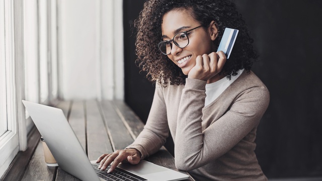 Happy woman holding payment card using a laptop