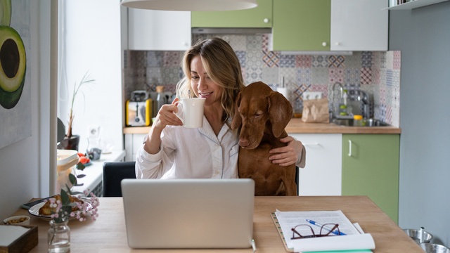woman having coffee at home on laptop with her dog