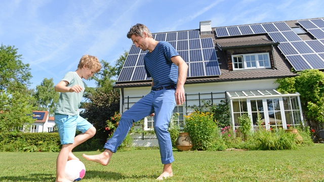 son and father playing in front of solar panel house