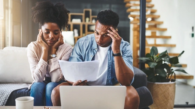 worried couple sat at a table looking at their laptop and paperwork