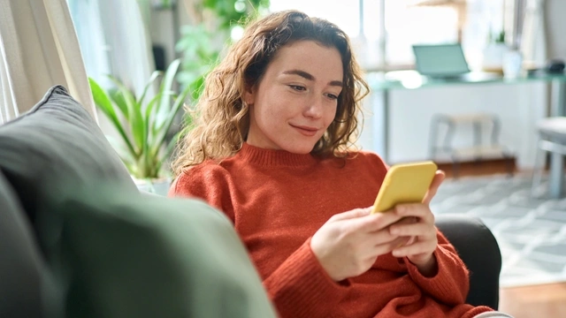 Happy young woman in red jumper using yellow phone