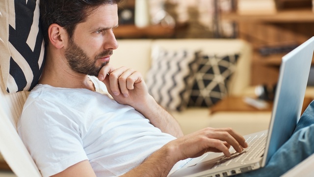 Thoughtful looking white man in t-shirt using laptop