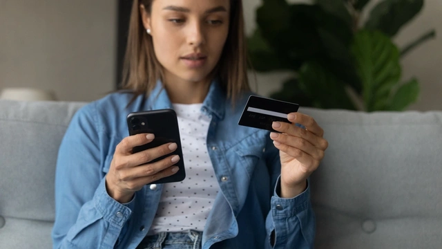 Woman looking at a credit card while holding a smartphone