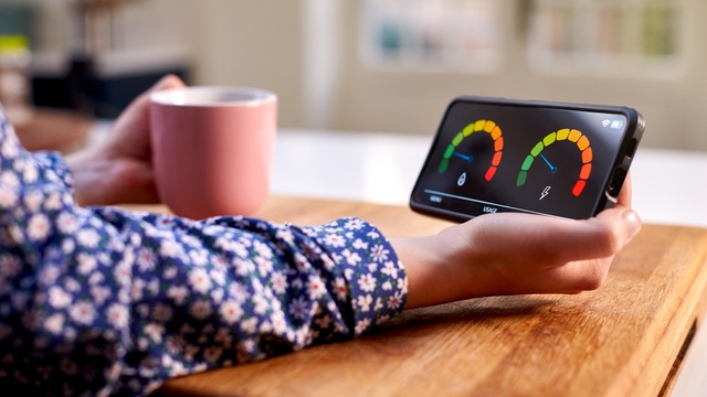 Lady in blue floral blouse holding pink mug and smart meter with two dials