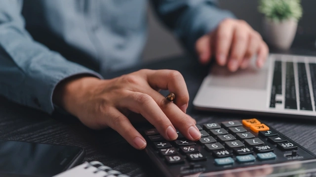 close up of a man on his laptop and using a calculator