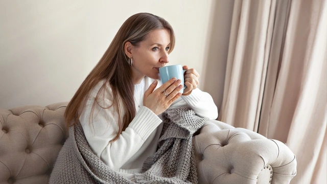 Woman sat on the sofa under a blanket drinking a hot drink