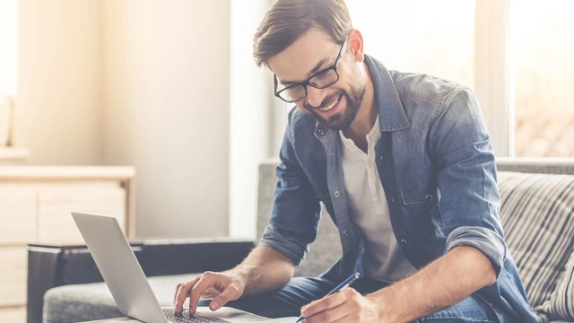 man on laptop smiling and making notes