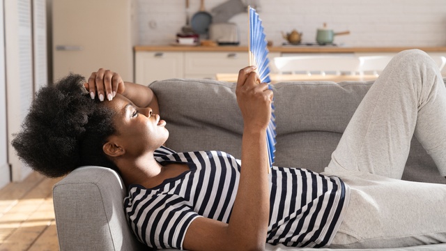 woman cooling down with a fan on sofa at home