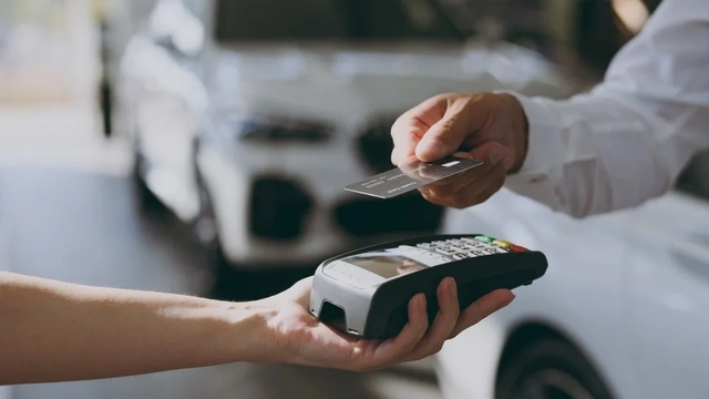 someone paying contactless with their credit card, with a car dealership in the background