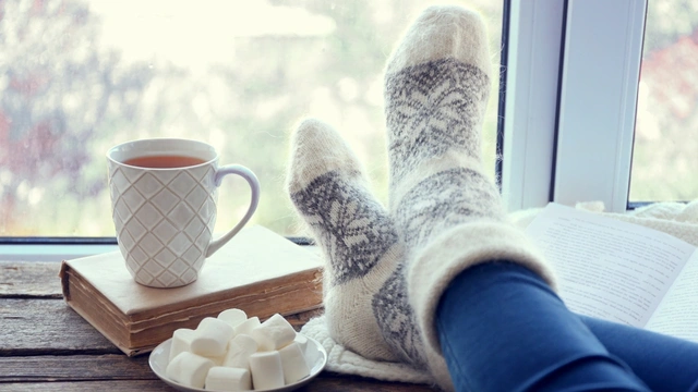 woman with feet up on window sill with a hot drink, book and marshmallows