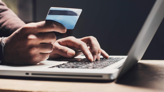Person holding a credit card while browsing on a laptop