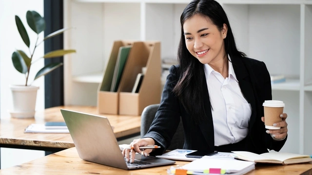 business woman holding a drink and working on her laptop