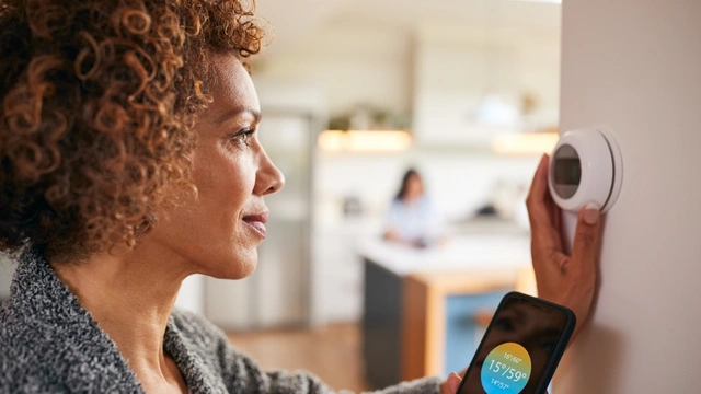 A lady with dark curly hair adjusts her thermostat