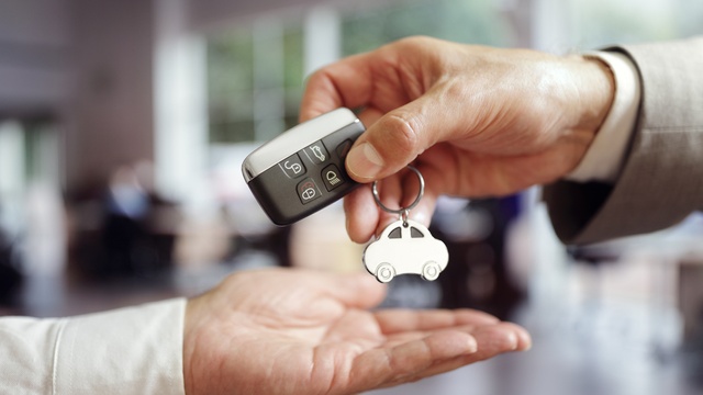One person hands a car key to someone else. Only their hands and the car key fob are visible.