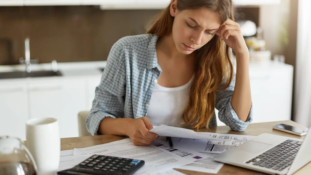 Woman sat at the table with her laptop and surrounded by paperwork, calculating debts