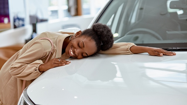 Happy lady hugging her new white car in the dealership