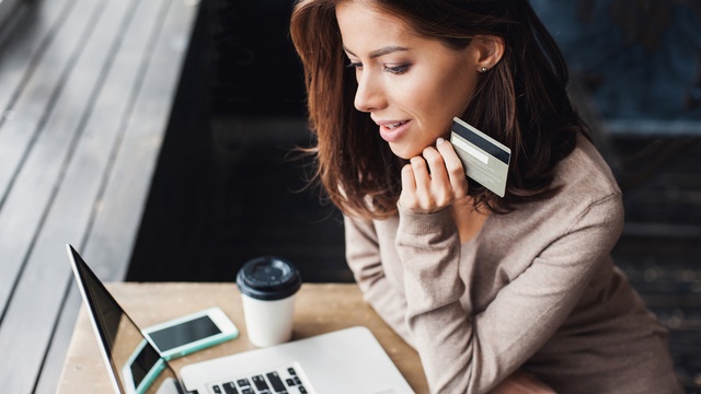 Young woman on her laptop in a coffee shop holding a credit card