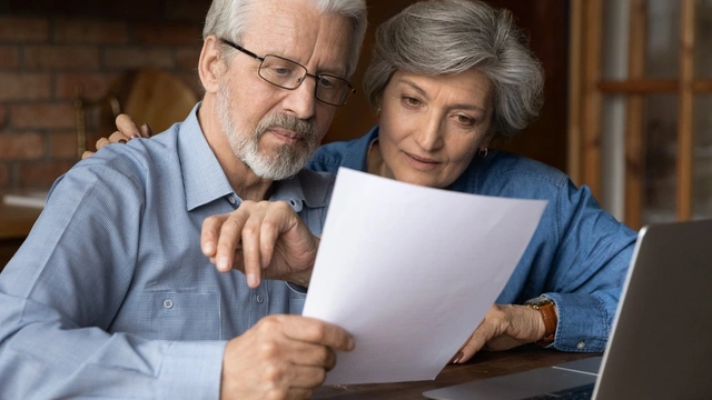 Older couple looking over a document with their laptop open