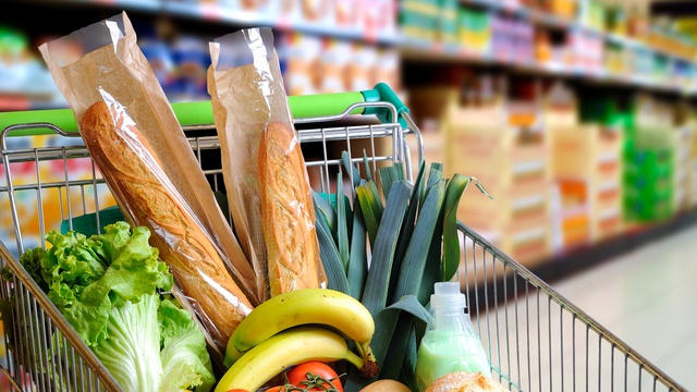 supermarket trolley with green handle filled with groceries including bananas, bread and greens