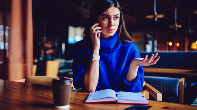 Woman talking on the phone at a table with a coffee cup