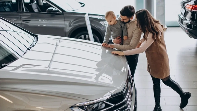 A young couple and their small child, looking at a used car in a dealership.