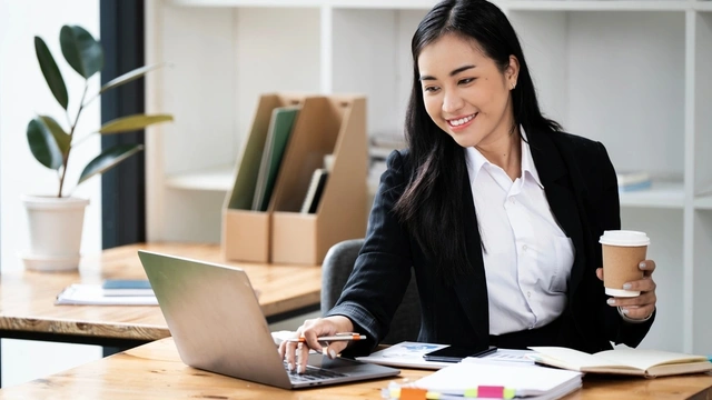 business woman holding a drink and working on her laptop