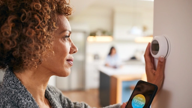 A lady with dark curly hair adjusts her thermostat