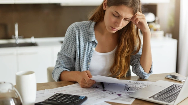 Woman sat at the table with her laptop and surrounded by paperwork, calculating debts