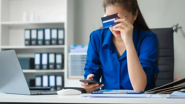 Woman looking at her phone and holding up a credit card