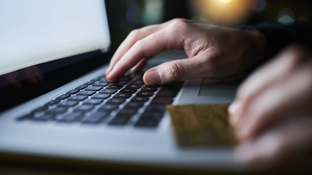 zoomed in on a man using a laptop with a credit card in his hand.