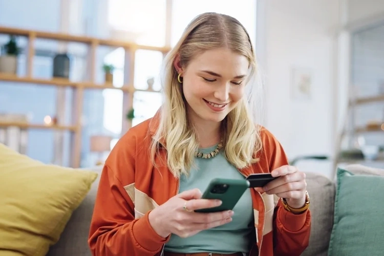 woman sat on her phone and holding her credit card