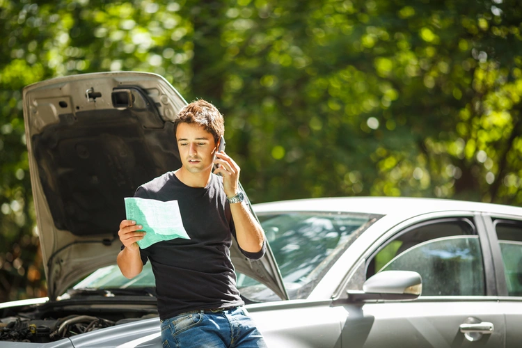 Man sat on broken down car, checking his car insurance policy over the phone 