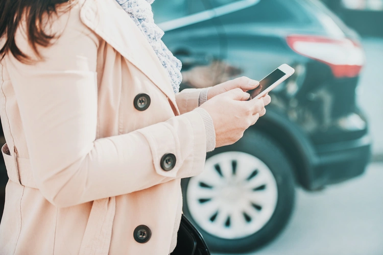 Woman using her phone in front of a parked car
