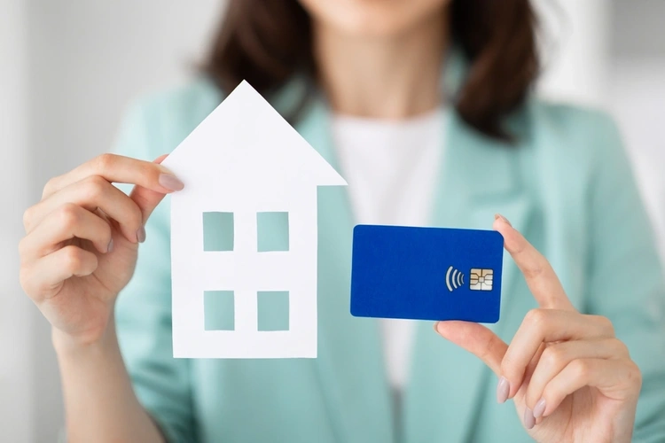 Close up of woman holding up a small house and a credit card