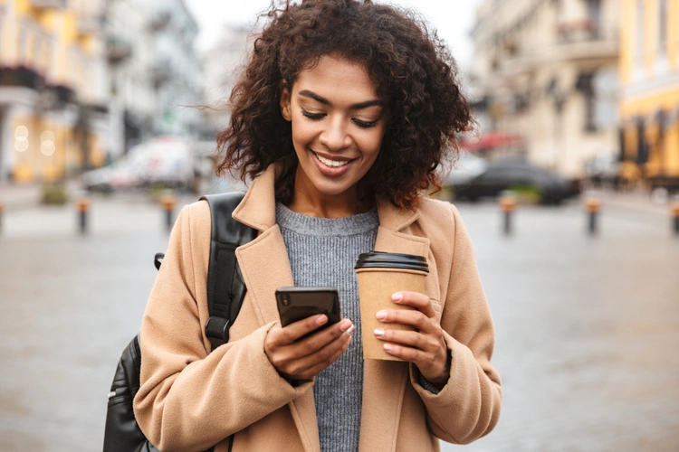 Woman checking her phone while holding a coffee cup