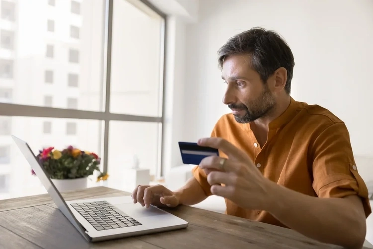 Man sat at his laptop with a credit card in his hand.