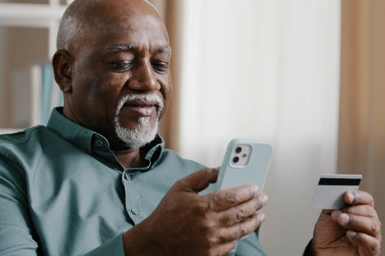 Older African man on mobile phone using credit card