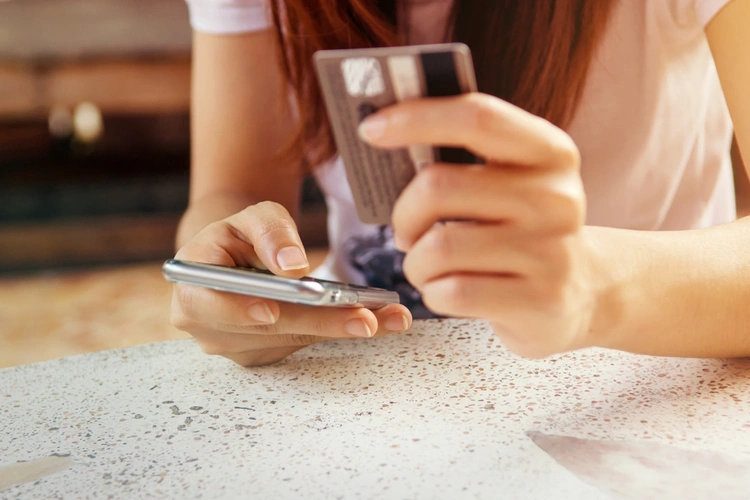 Person purchasing something online, holding their phone and credit card