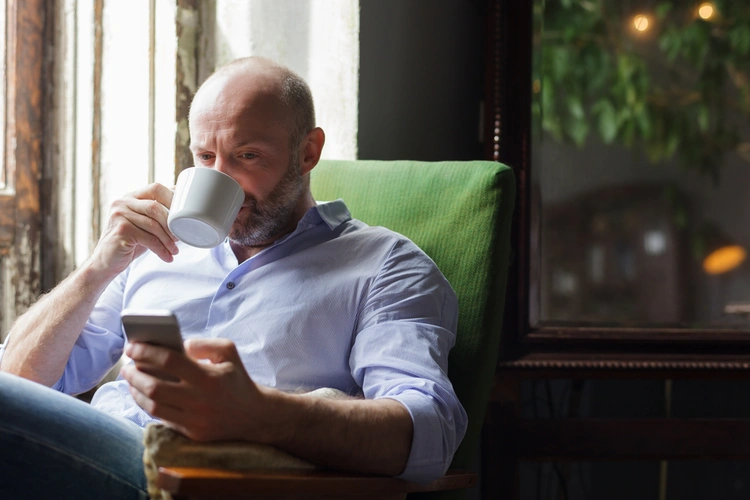 Man sipping from a mug while looking at his phone